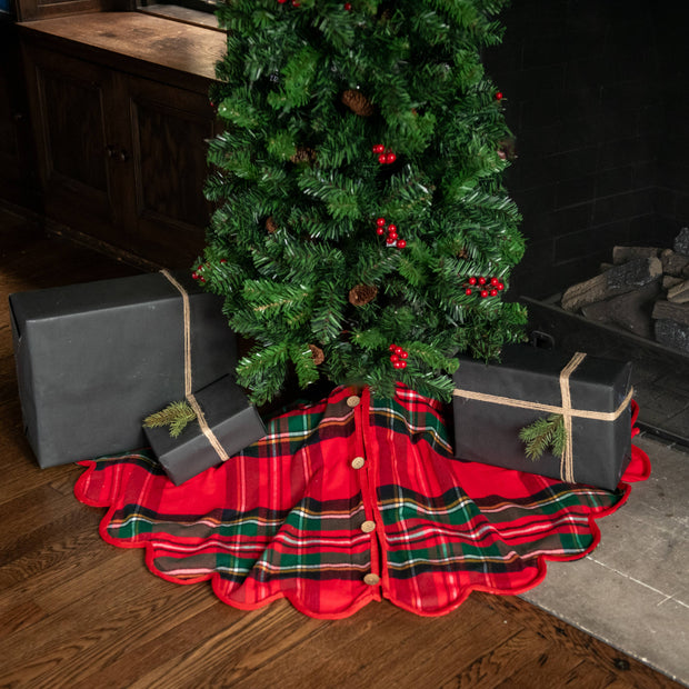 Decorated Christmas tree with a red plaid skirt and presents underneath, next to a fireplace.