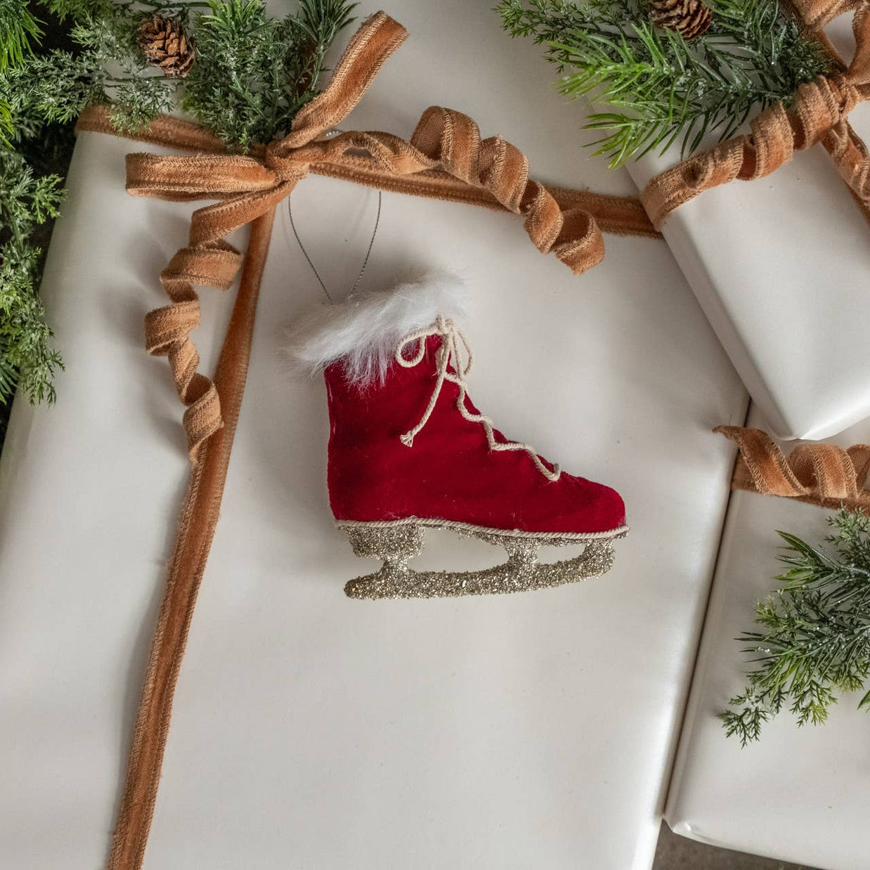Red ice skate ornament on white paper with brown ribbon and greenery