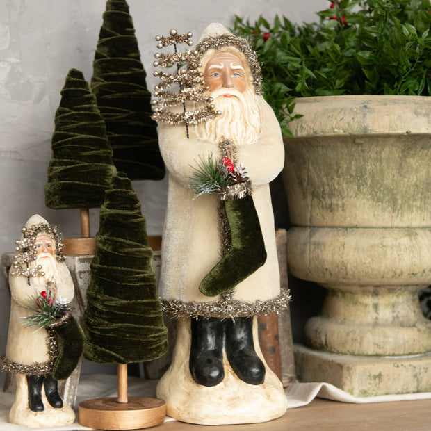 Decorative Santa Claus figure with a green stocking in front of small trees and a pot.
