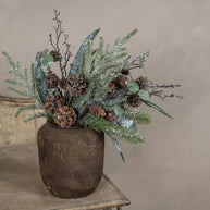 Decorative arrangement with greenery and pinecones in a rustic pot on a neutral background