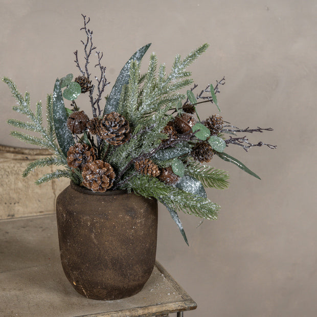 Decorative arrangement with greenery and pinecones in a rustic pot on a neutral background