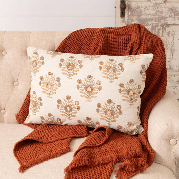 Decorative pillow with floral pattern on a beige sofa with a rust-colored throw blanket.