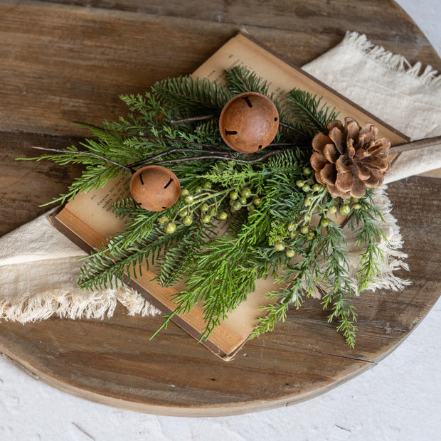 Decorative arrangement with greenery, pinecones, and bells on a wooden surface.
