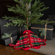 Small Christmas tree with a plaid skirt draped over it, surrounded by black gift boxes.