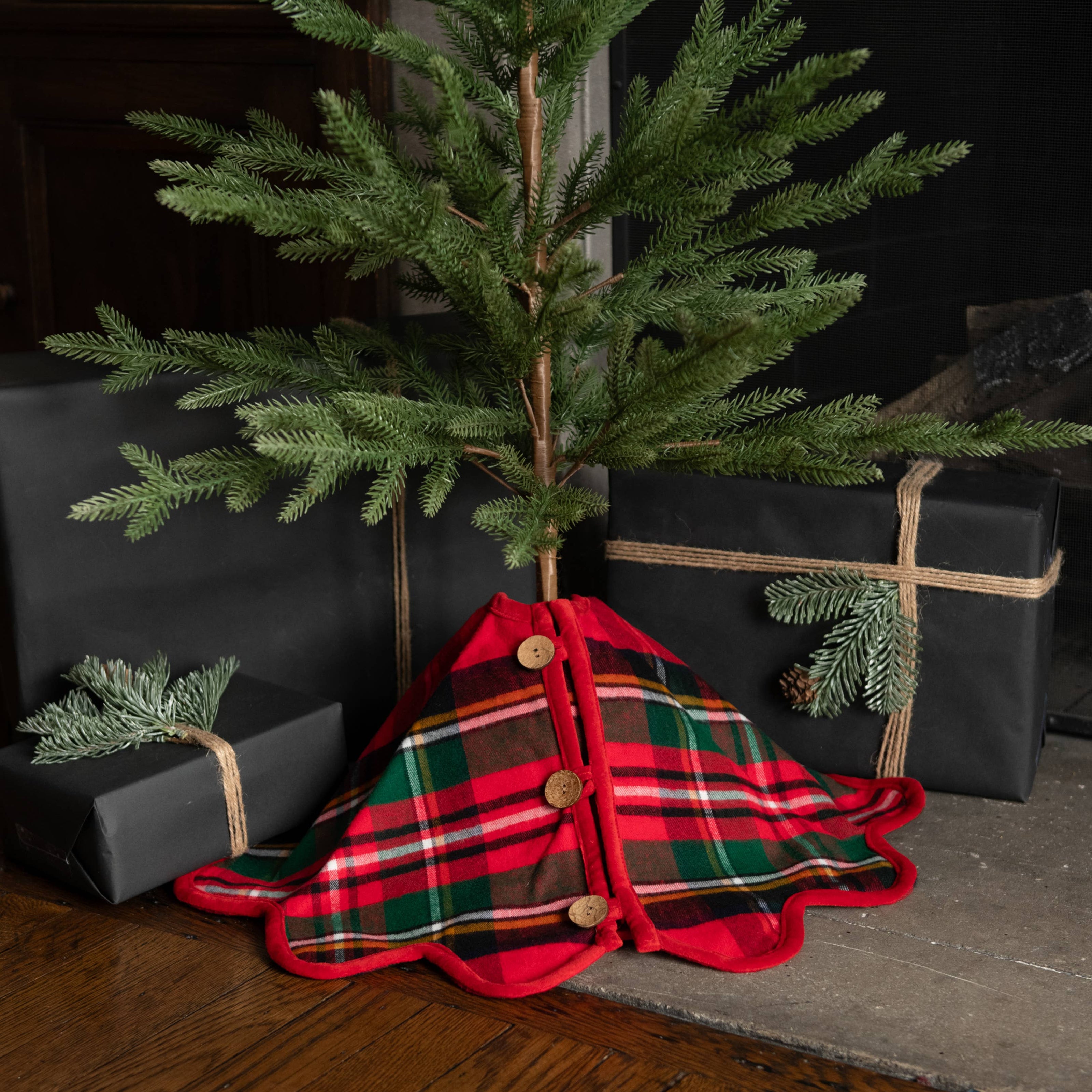 Small Christmas tree with a plaid skirt draped over it, surrounded by black gift boxes.