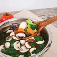 Stir-fry dish with vegetables on a wooden spoon over a pot of soup.