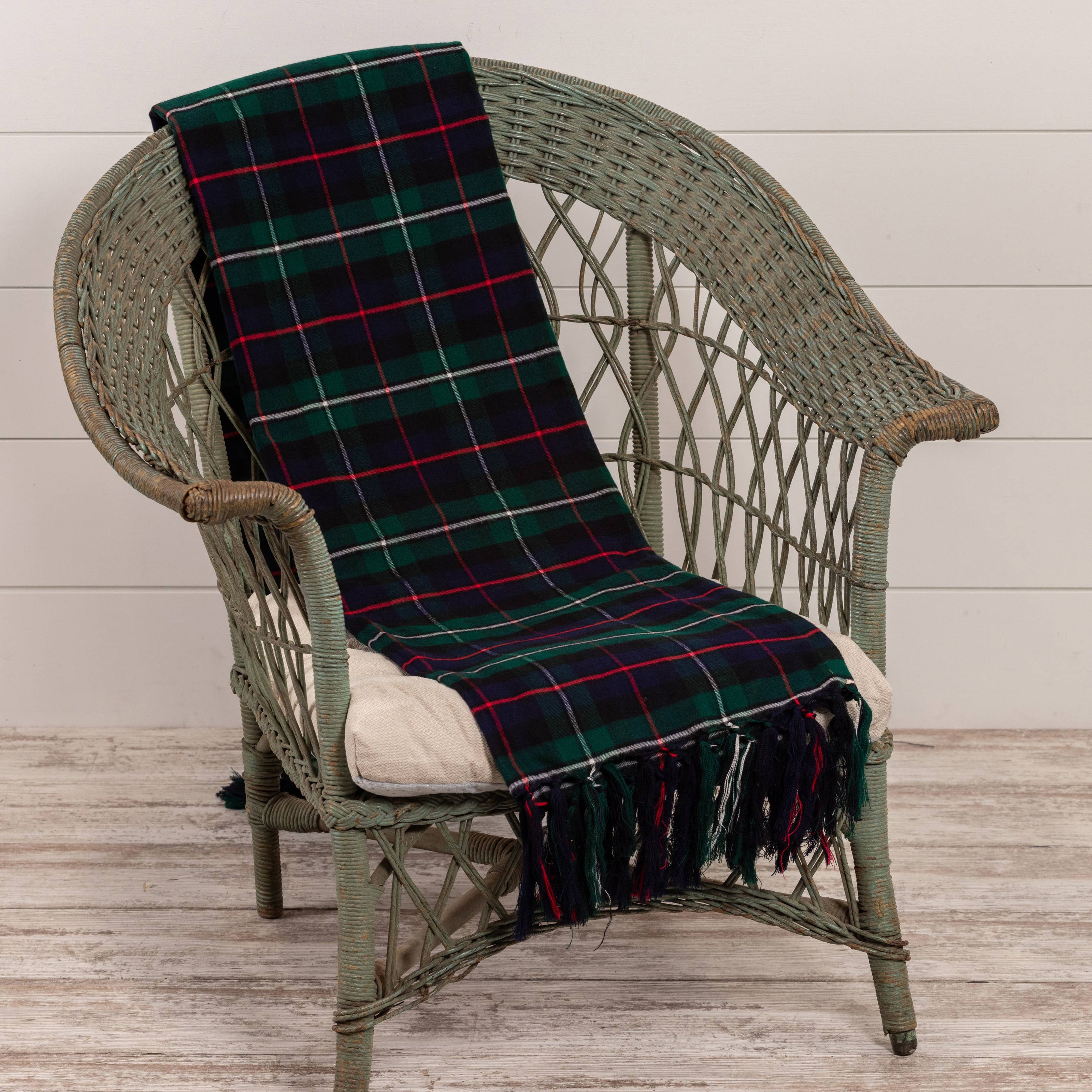 Plaid blanket draped over a wicker chair with a white cushion on a wooden floor.