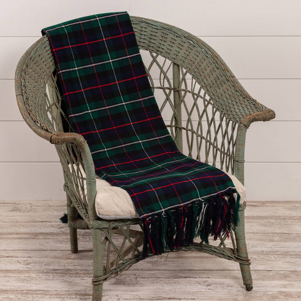 Plaid blanket draped over a wicker chair with a white cushion on a wooden floor.