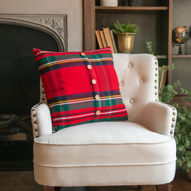 Beige armchair with a red plaid pillow in a cozy room setting.