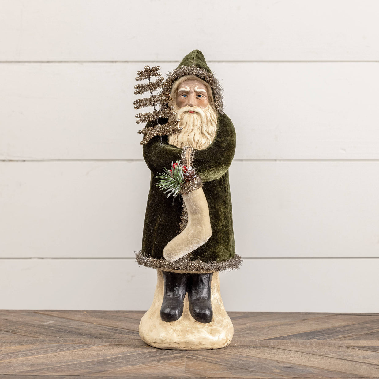 Decorative figure of a bearded man in a green coat holding a tree against a white wooden background.