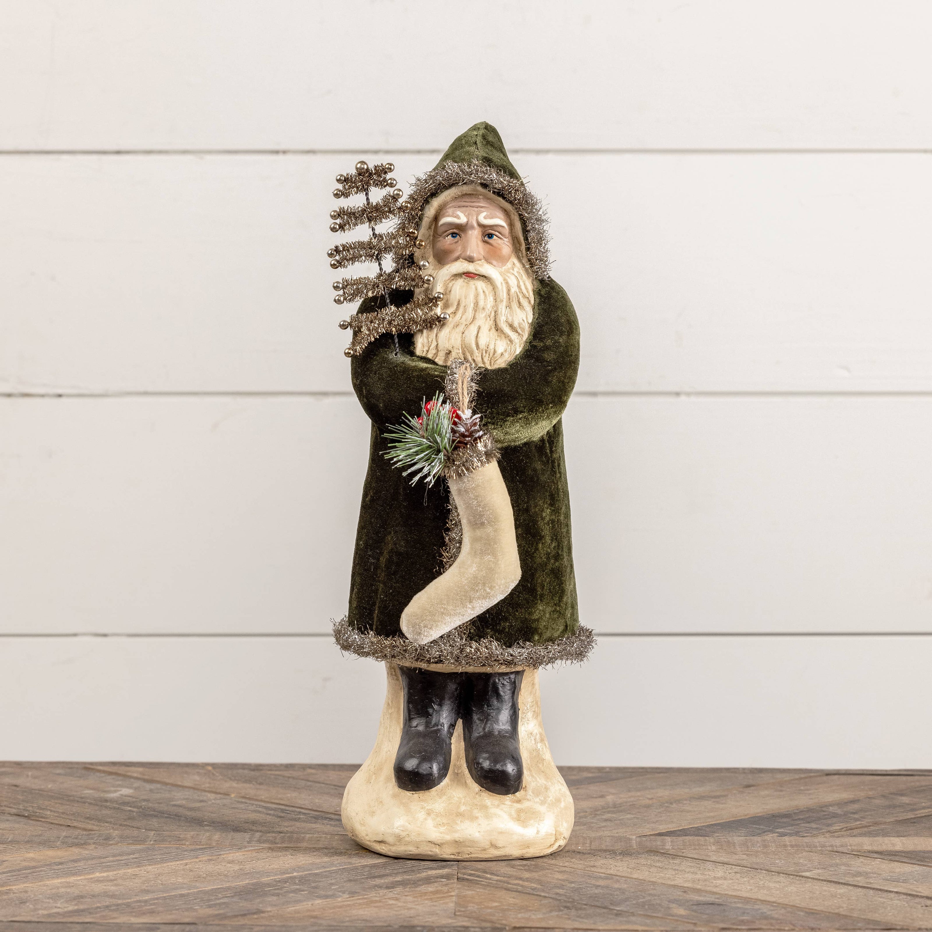 Decorative figure of a bearded man in a green coat holding a tree against a white wooden background.