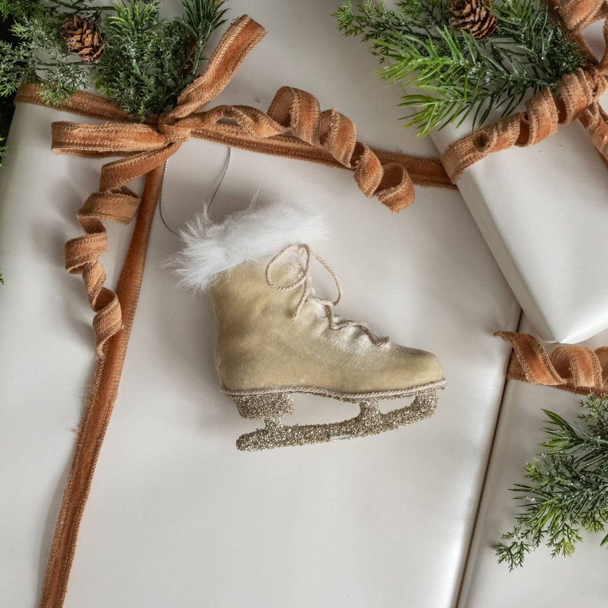 Decorative ice skate ornament on a wrapped gift with brown ribbon and greenery.