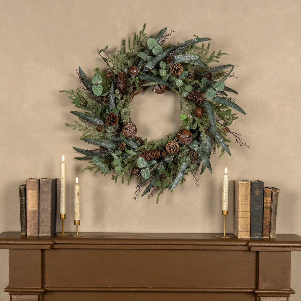 Decorative wreath with greenery and pinecones on a wooden surface with candles and books.