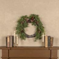 Green wreath with pinecones on a beige wall above a wooden console table with books and candles.