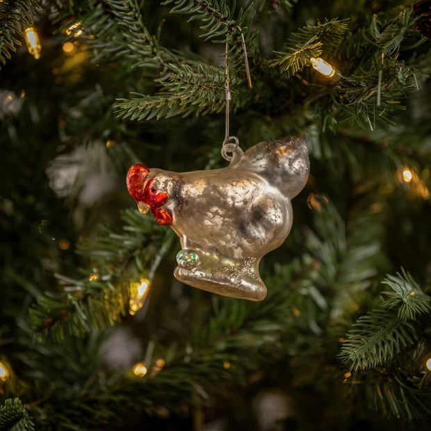 Decorative glass chicken ornament hanging on a Christmas tree with lights.