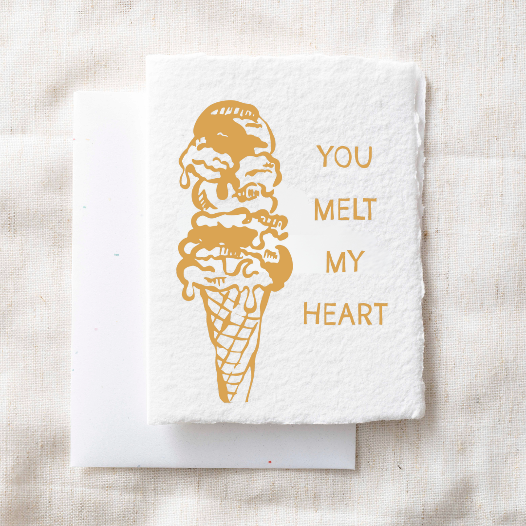 White towel with gold ice cream cone and 'You Melt My Heart' text on a beige fabric background