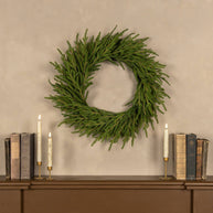 Green wreath on a wall above a wooden shelf with books and candles.