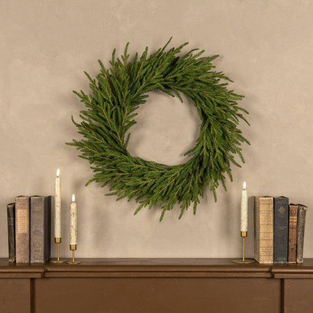 Green wreath on a wall above a wooden shelf with books and candles.