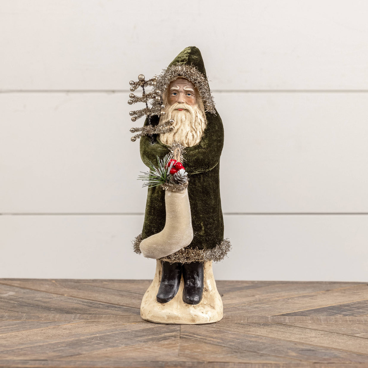 Decorative figure of a bearded man in a green coat holding a tree on a wooden surface with a white background