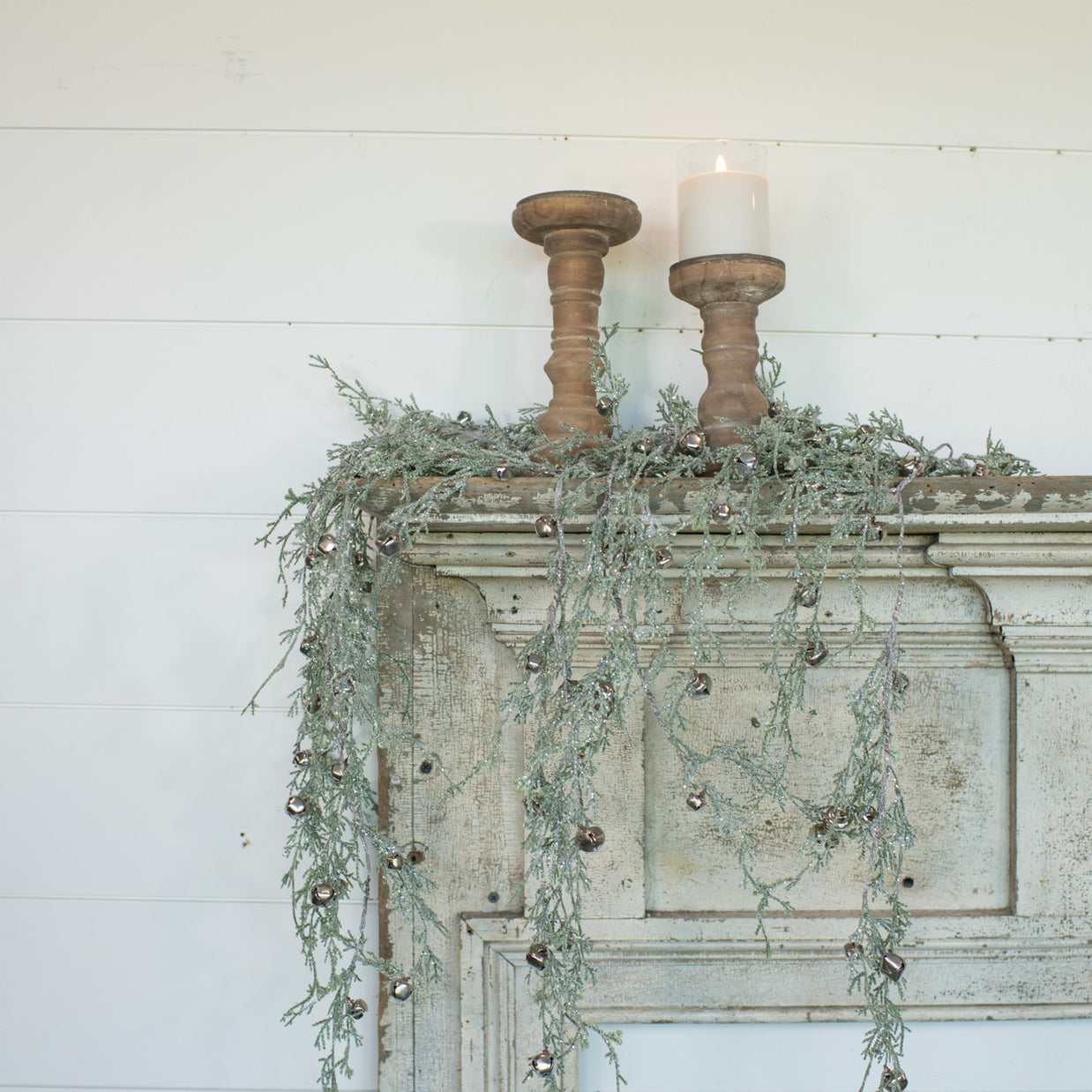 Decorative mantel with wooden candle holders, candles, and greenery against a white wooden wall.