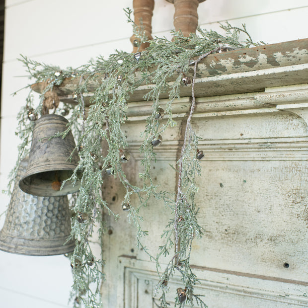 Decorative hanging with greenery and metal bells against a rustic wooden background