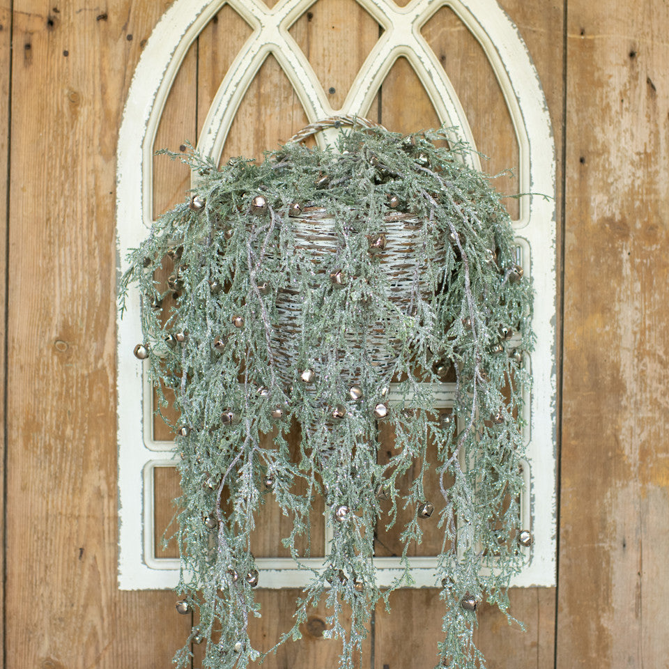 Decorative wreath with greenery and small balls hanging on a wooden door with a decorative arch.