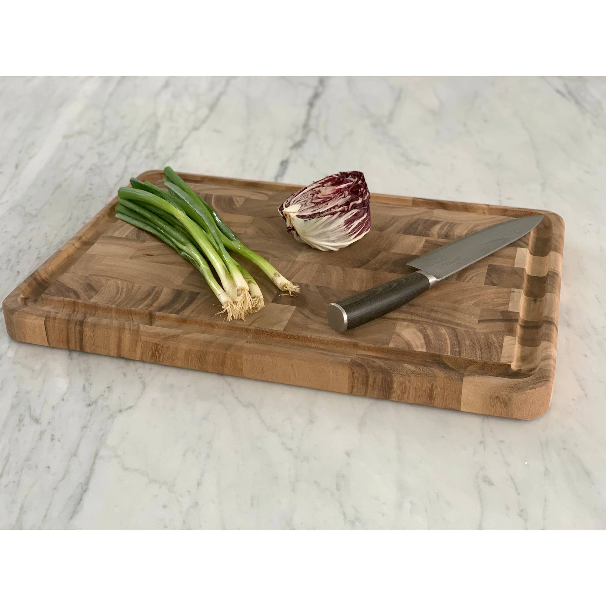 Wooden cutting board with knife, green onions, and radicchio on a marble surface