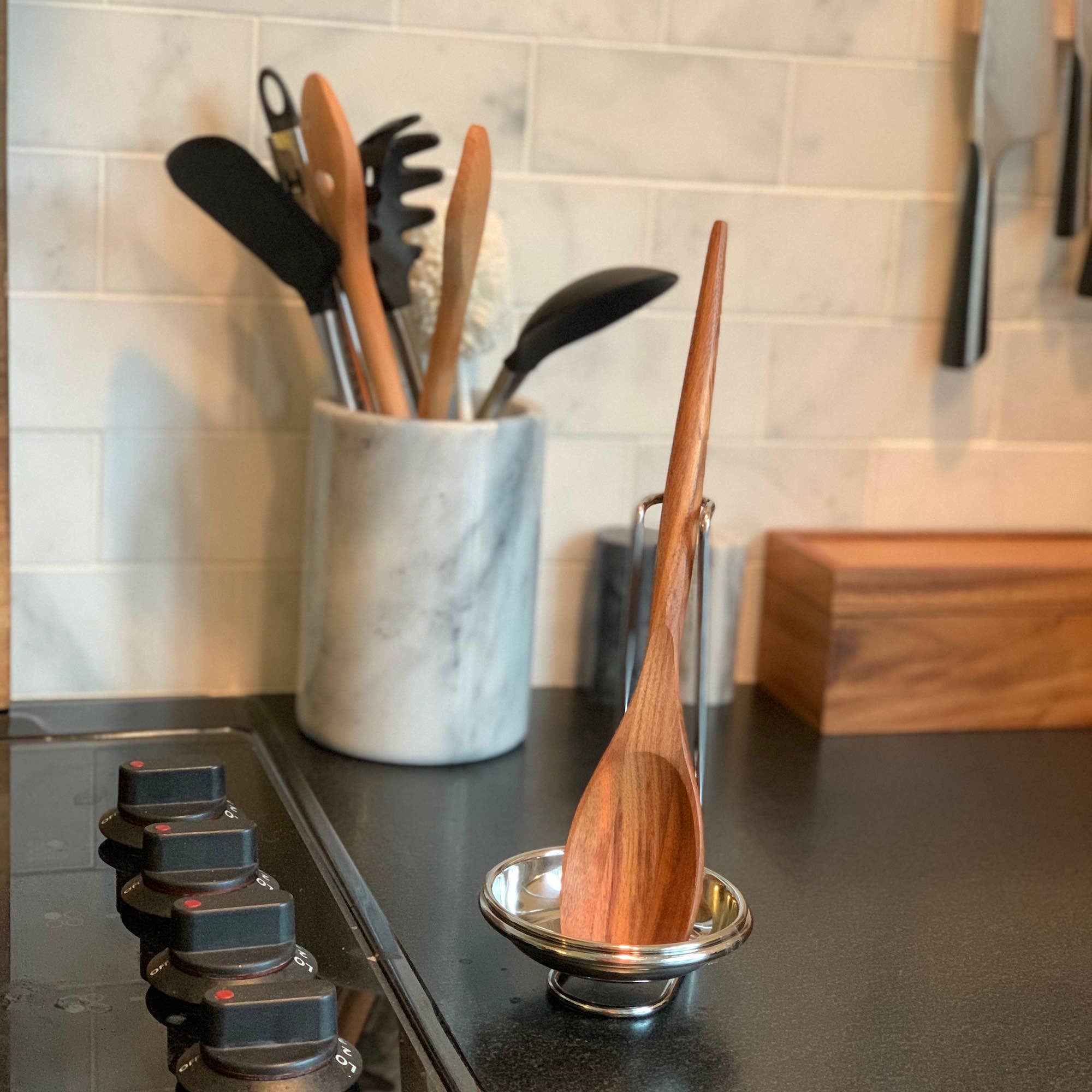 Wooden spoon on a stand with a marble utensil holder in the background on a kitchen counter.