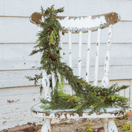 Decorative chair with a green garland against a white wooden wall.