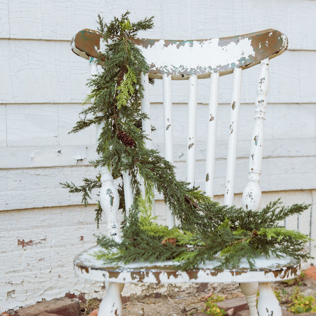 Decorative chair with a green garland against a white wooden wall.