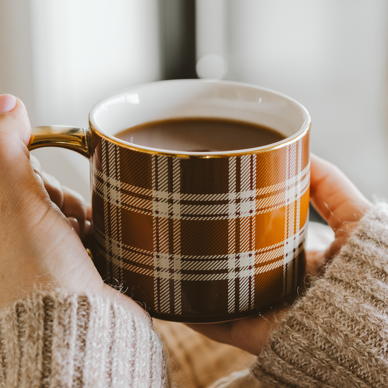 Person holding a plaid mug with coffee in a cozy setting