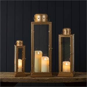 Set of three gold lanterns with candles inside on a dark background