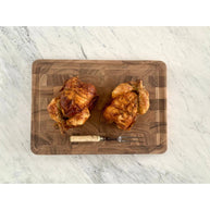Two roasted chickens on a wooden cutting board with a marble background
