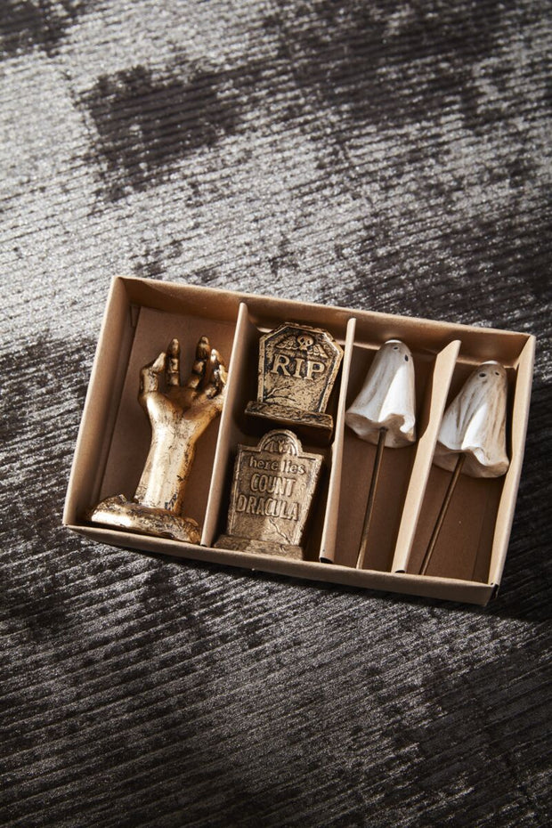 Decorative items including a hand, tombstone, and skull in a box on a textured surface.