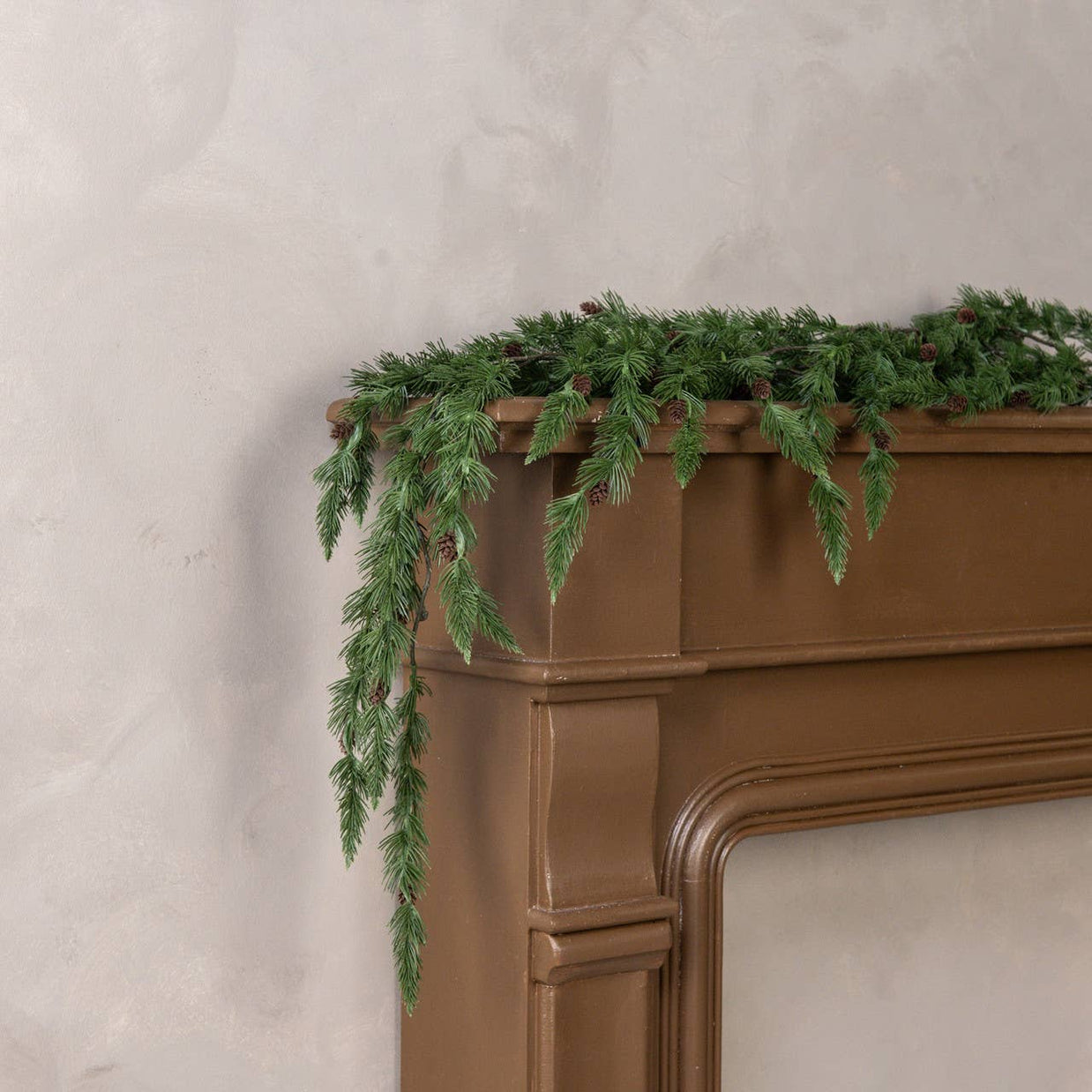Green fireplace mantel garland on a brown fireplace against a light gray wall.