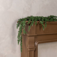 Green fireplace mantel garland on a brown fireplace against a light gray wall.
