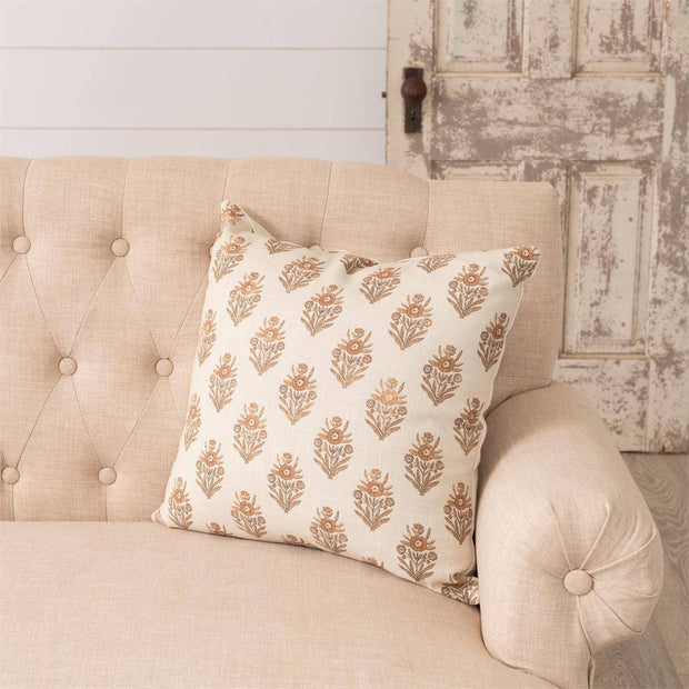 Decorative pillow with floral pattern on a beige sofa against a rustic wall.
