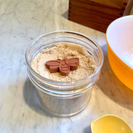 Clear jar with powder and a bee-shaped object on a marble surface