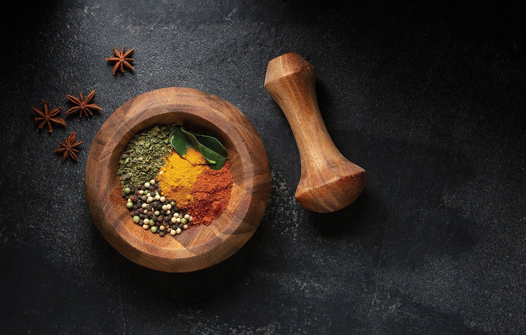 Wooden bowl with spices and a wooden pepper grinder on a dark surface