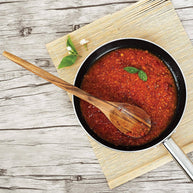 Red sauce in a black pan with a wooden spoon on a wooden surface
