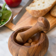 Wooden mortar and pestle with almonds on a marble surface, surrounded by bread, an apple, and salad.