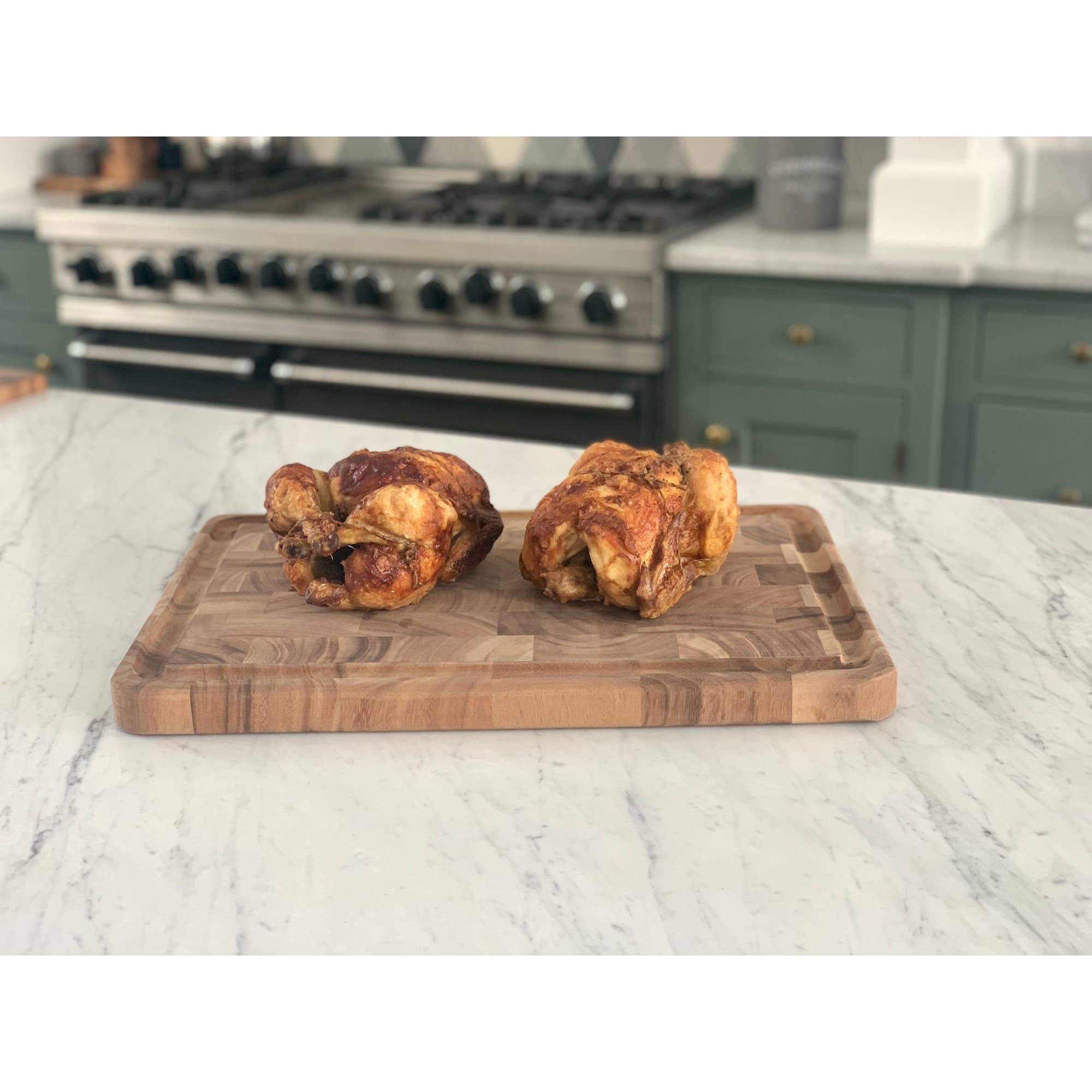 Two roasted chickens on a wooden cutting board in a kitchen setting.