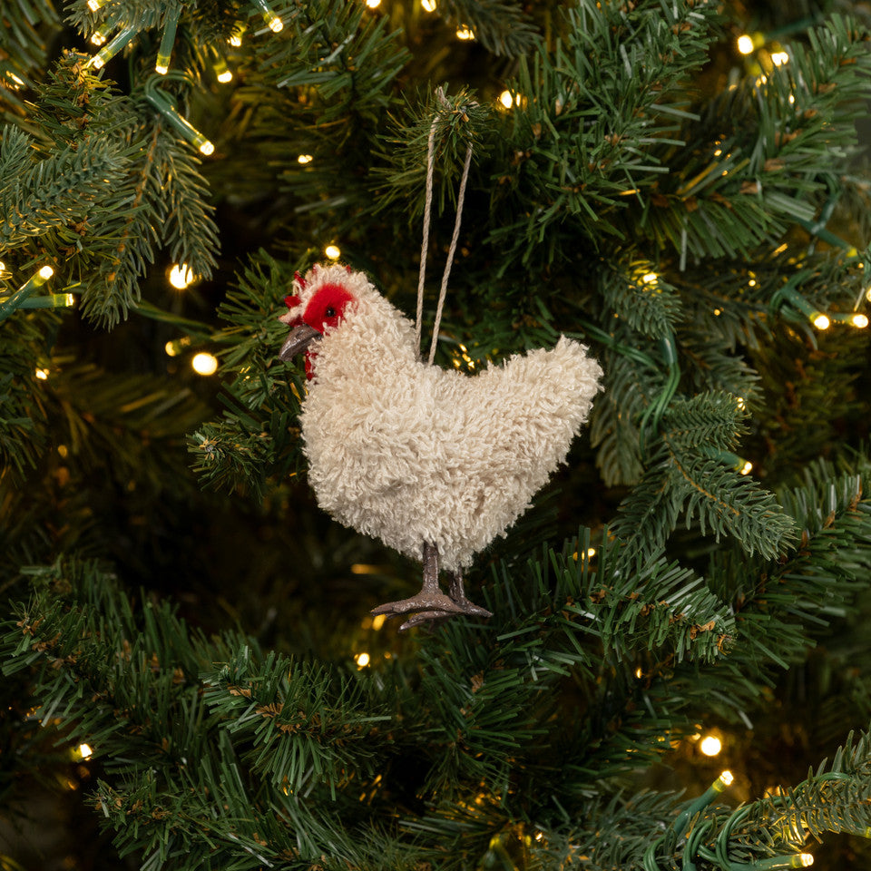 Decorative chicken ornament hanging on a Christmas tree with lights.