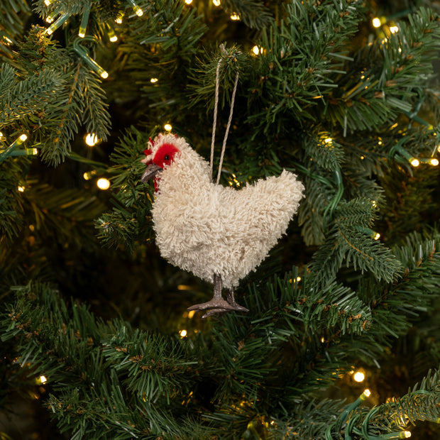 Decorative chicken ornament hanging on a Christmas tree with lights.
