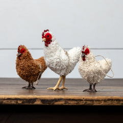 Three decorative chicken figures on a wooden surface with a light gray background