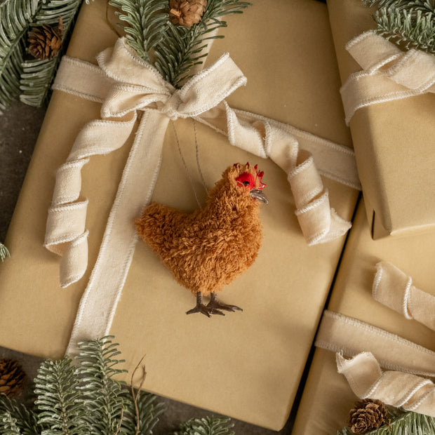 Small brown chicken figurine on a wrapped gift with beige ribbon and greenery.