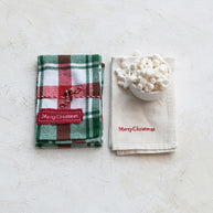 Two Christmas-themed napkins with 'Merry Christmas' text on a light surface.