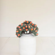 Small wreath with orange flowers on a white vase against a plain background