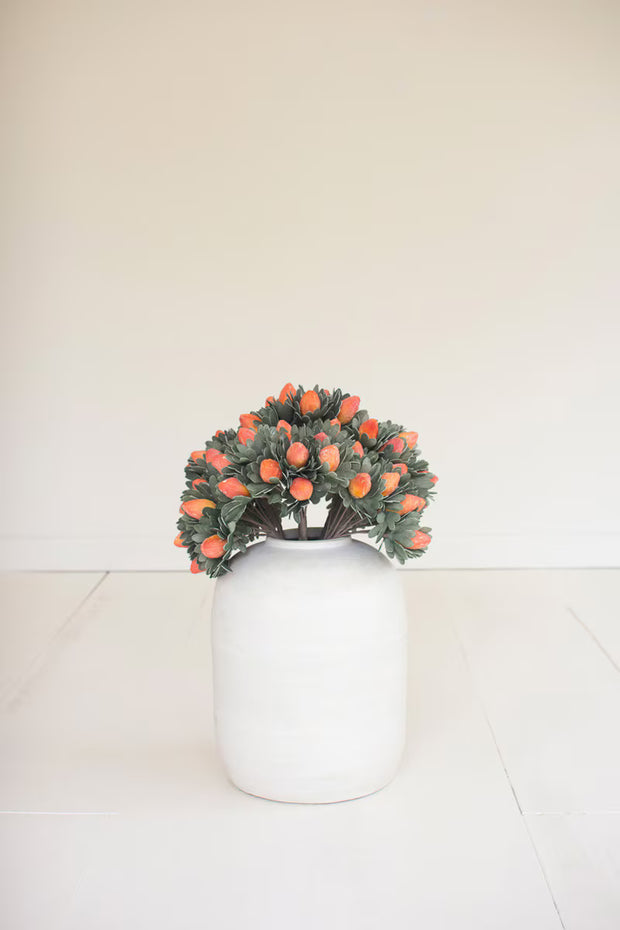 Small wreath with orange flowers on a white vase against a plain background