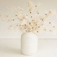 White vase with dried flowers on a light wooden floor